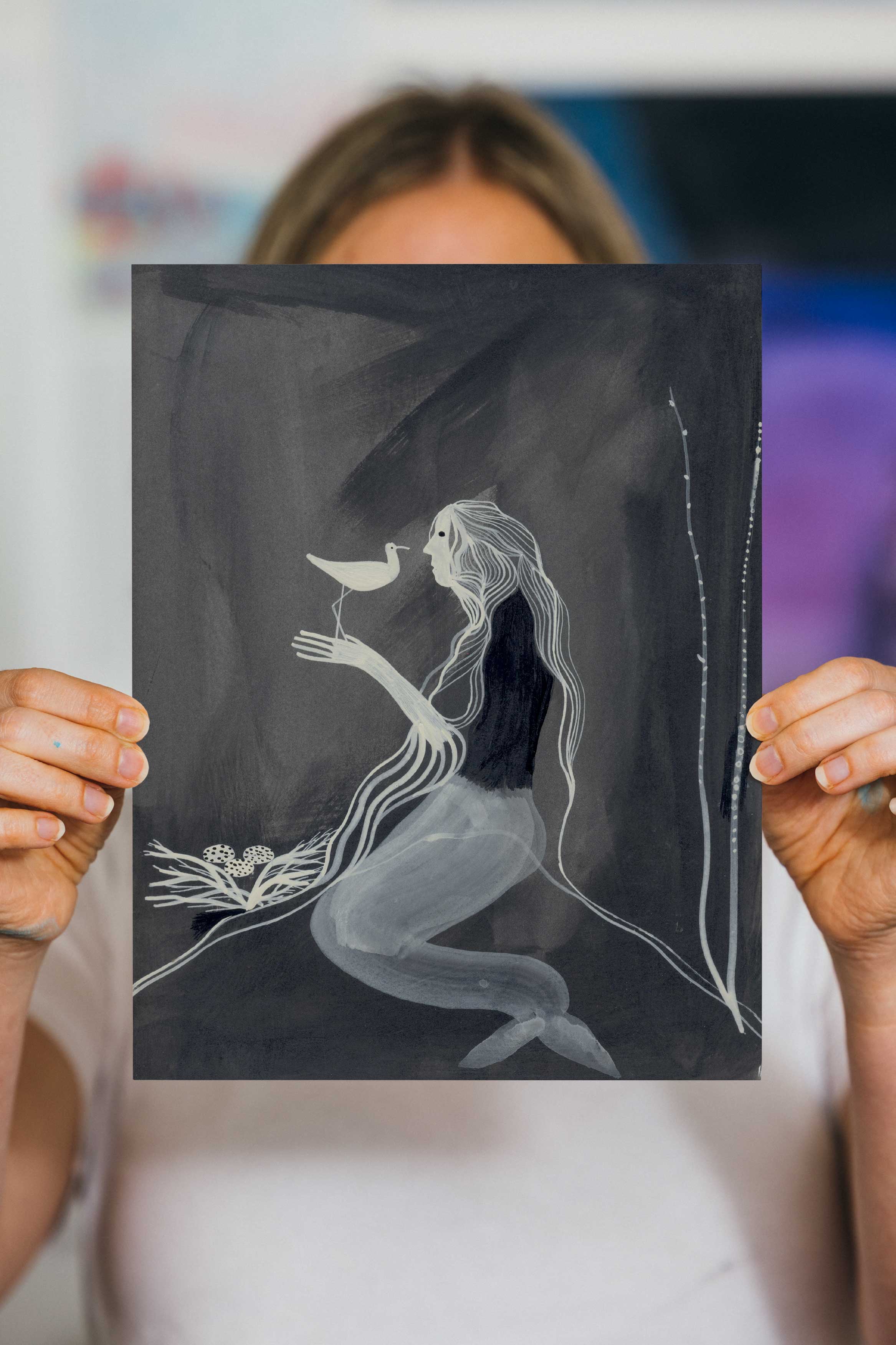 Person holding a black and white drawing of a mermaid holding a bird